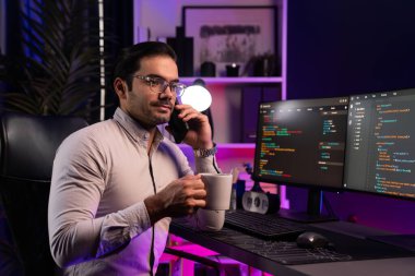 Akıllı bilişim geliştiricisi elinde kahve fincanı olan bir iş arkadaşını arıyor. Bilgisayar ekranında yazılım geliştirme kodlaması yapıyor. Program güncellemesini neon aydınlatma ofisinde sunuyor. Tahmin et..