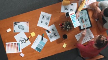 Proje yöneticisi renk paletleri seçerken tasarımcının tablete baktığı yukarıdan aşağıya hava görüntüsü. Profesyonel grafik tasarımının en üst görüntüsü ve logoya bakın. Yetenekli ekip grafikleri seçiyor. Sempozyum.