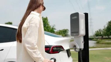 Genç kadın elektrik şebekesine bağlı elektrik şebekesine bağlı EV araba aküsünü elektrik endüstrisi olarak şarj ediyor. Çevre dostu araç kullanımı için. Yararlı