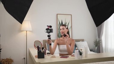 Sosyal medya için güzellik ve kozmetik video içeriği hazırlayan genç bir kadın. Güzellik blogcusu kameraya gülümserken seyircilere ve takipçilere güzellik bakımını gösteriyor. Düzenle