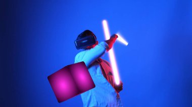 Parlayan kılıcı tutan ve VR gözlük takan oyuncu oyun oynuyor. Çekici erkek model sanal gerçeklik gözlüğü kullanarak yüzen bloğu eskrirken heyecanlanıyor. Teknoloji yeniliği. Aygıt.