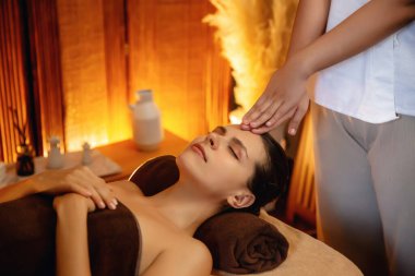 Beyaz kadın stres önleyici kafa masajı yapmaktan ve lüks otel veya otelde sıcak mum ışığında yüz güzelliği eğlencesi yapmaktan zevk alıyor. Sessiz.