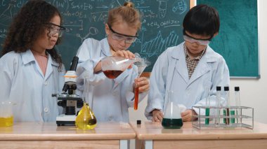 Kafkasyalı öğrenci deney yapıyor ve laboratuvarda yeni yenilikler keşfetmek için bekleyen meraklı çocuklarla çevrili biyokimyasal solüsyon döküyor. Çeşitli mutlu öğrenciler deney yapıyor. Pedagoji.