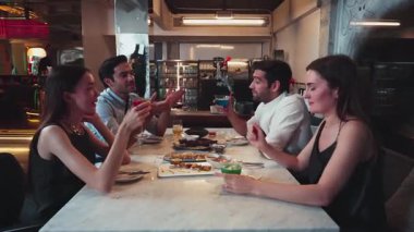 Grup arkadaşının kokteyl içkileriyle tezahürat yapmak. Etrafı ızgara ve kızarmış et menüsüyle çevrili. Birlikte lüks bir restoranda yemek masasında eşsiz bir şef masası menüsü var. Vinosity.