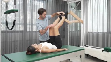 Pilates hocası, Cadillac teçhizatı üzerindeki bacak kaldırma egzersizi sırasında bir müşteriye yardım ediyor. Öğrenci uzanıyor ve temel dayanıklılık ve bacak esnekliğini arttırmak için Cadillac 'ın üzerinde bacak daire çiziyor. Alışkanlık.