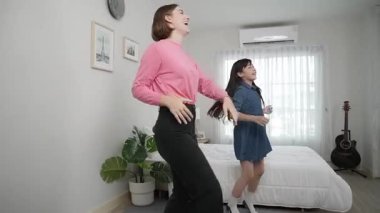 Yatak odasında Asyalı kızıyla müzik eşliğinde dans eden mutlu çekici anne. Beyaz anne dans eder ya da egzersiz yapar. Bu arada tatlı çocuk da müzik eşliğinde yatağa atlar. Aile eğlence konsepti. Pedagoji.