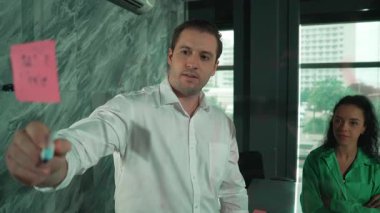 Yetenekli işadamı, cam duvara renkli yapışkan notlar yapıştırarak proje yöneticisine pazarlama fikrini sundu. Proje yöneticisi yatırımcıya projeyi gösteriyor, anlatıyor, gösteriyor. Yönlendirici.