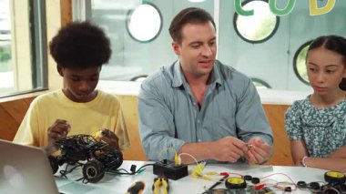 Akıllı akıl hocası araba modelini tamir ederken elektronik aletleri öğretiyor. Kafkas öğretmeni masadaki dizüstü bilgisayarlı robot inşaatı açıklarken, araba modeli etrafa saçılmış. Öğretim