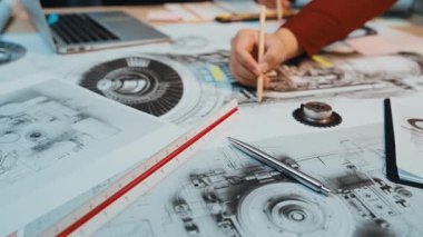 Odaklanmış bir birey, mühendislik ve tasarım projeleri için gerekli araç ve cihazlarla çevrili modern bir çalışma alanında karmaşık teknik çizimleri inceler. SACTR