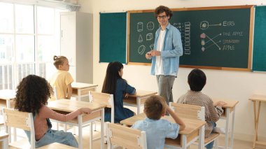 Çeşitli ilkokul öğrencileri öğretmenleri çocuğa bakarken sınıfta yürüyorlar. Profesyonel eğitmen tahtaya çıkıp öğretmenlik yapmaya hazırlanırken sevimli çocuklar sınıfa katılıyor. Pedagoji.