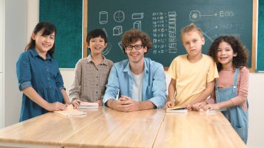 Profesyonel Kafkas öğretmeni ve çeşitli öğrenciler kameraya bakarken mutlu okul çocuğu gülümsüyor. Sınıfın önünde dururken gülümseyen bir grup çok kültürlü çocuk. Eğitim. Pedagoji.