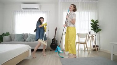 Beyaz anne ve Asyalı çocuk birlikte ev işi yapıyor ve müzik eşliğinde dans ediyorlar. Çekici anne ve kız modern yatak odasını temizlerken şarkı söyleyip rahatlatıcı müziğe atlıyorlar. Yaşam tarzı. Pedagoji.