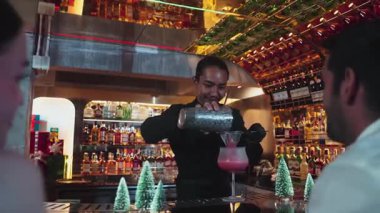 Asyalı barmen alkollü likör ve şerbetli kokteyl bardağıyla süslenmiş noel ağaçlarında gece kulübündeki VIP çiftlere taze içecek servisi yapıyor. Vinosity.