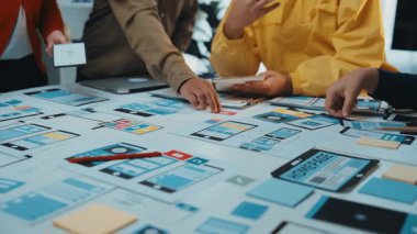 Çeşitli bir ekip, cihazlar ve renkli notlarla çevrili mobil uygulama tasarımı üzerinde işbirliği yapar. Canlı çalışma alanı teknoloji gelişimindeki yaratıcılığı ve yeniliği yansıtıyor. SACTR