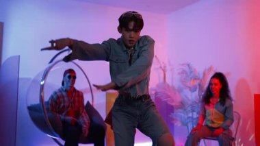 Çok kültürlü bir arkadaş kürsüde otururken Asyalı yetenekli bir dansçı modern müziğe geçiyor. Profesyonel dansçı, hipster takımı tezahürat yaparken ve desteklerken enerjik adımlar atıyor. Mutluluk.