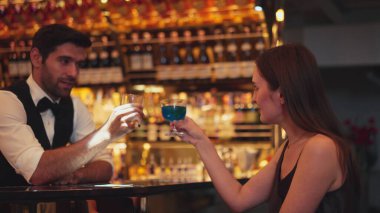 Gülümseyen güzel bir kadın konuğun yanında canlı bir şekilde zeki bir barmenle oturup cuma günkü kulüpte lüks tezgah barında mavi Hawaii kokteyli ve viski içerken. Vinosity.