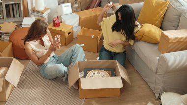 Lezbiyen aşıklar taşınma gününde karton kutudan nesneleri alıyorlar. Taşınırken paketleri açmak ve kutudan mobilya toplamak için birlikte çalışan bir çift oda arkadaşı. Yer değiştirme konsepti. Myrmidon.