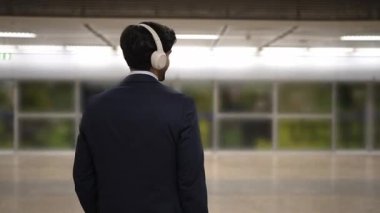 İş adamı, peronda arka planı bulanık bir şekilde tren beklerken kulaklıktan müzik dinliyor. Proje yöneticisi cep telefonu tutarken dinlenme sesi dinlemeyi sever. Sevinçli..