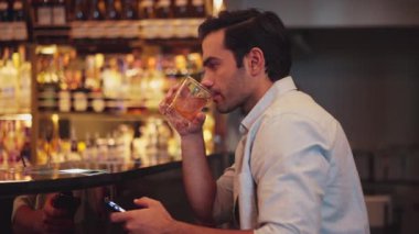 Akıllı adam, cuma gecesi lüks bir bar ve restoranda gece kulübünün karşılama barında arkadaşlarıyla sohbet ederken tek başına kokteyl içiyor. Vinosity.