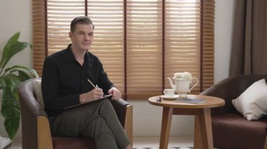 Psikiyatri ofisinde ya da terapi odasında koltukta oturan erkek psikolog. Arkadaş canlısı ve profesyonel ruh sağlığı danışmanı ve terapisti. Düzenle