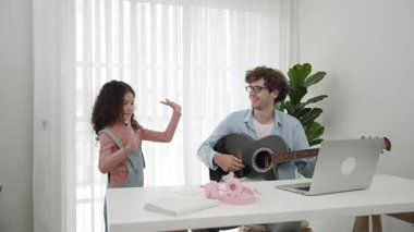 Çekici beyaz bir baba gitar çalarken tatlı bir kız müzik eşliğinde dans ediyor. Mutlu baba ve Amerikalı kız birlikte vakit geçirirken akıllı çocuk müzik yapıyor. Aile eğlence konsepti. Pedagoji.