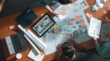 Planı elinde tutan inşaat mühendisi ekibinin en iyi görüntüsü ve dizüstü bilgisayar, proje planı ve planıyla masada duruyor. Yapışkan notları planlayan ve yazan yetenekli proje yöneticisinin havadan görünüşü. Sempozyum.