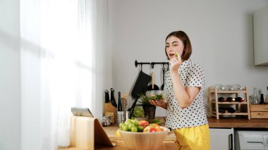 Kafkaseli anne kahvaltıda sebze pişirirken mutlu anne de modern mutfakta salata için taze malzemeler hazırlıyor. Hizmetçi sağlıklı yemek pişiriyor. Dikkat konsepti. Pedagoji.