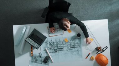 Dizüstü bilgisayarda çalışırken mimari çizimlerin hava görüntüsü. Kafkasyalı mühendisin bina modelini tasarlayıp, ekipman ve güvenlik kaskıyla birlikte tasarladığına dair tepeden aşağı bir bakış açısı. Hizalama.