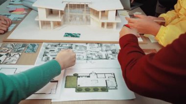 Canlı bir çalışma alanı, mimarları ve müşterileri bir tasarım toplantısına katılırken, bir masaya dizilmiş plan ve modelleri analiz ederken, yaratıcılığı ve işbirliğini teşvik ederken gösteriyor. SACTR