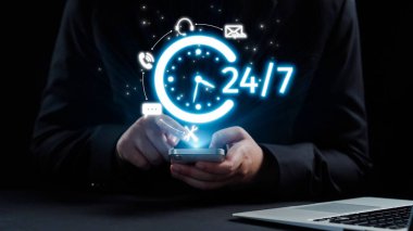 Bir kişi, modern bir iş bağlamında iletişim ve destek için 24 saatlik kullanılabilirliği sembolize eden dijital bir saat sergileyen bir akıllı telefondan yararlanıyor. Dörtgen