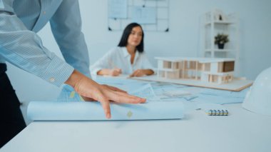 Ev modeliyle çalışan yetenekli beyaz tasarımcı Asyalı mimar mühendis ile toplantı masasında üzerinde taslak ve ev modeli dağınıklığı olan ev planlarını tartışırken. Tertemiz..