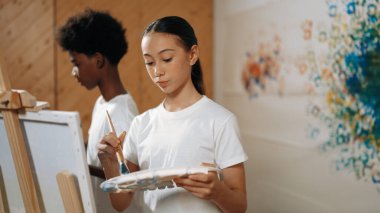 Çok kültürlü bir öğrenci resim dersinde tuvali renkli duvarlarla boyar. Afrikalı bir erkek ve beyaz bir kız resim çiziyor ya da birlikte yaratıcı aktiviteler yapıyor. Öğretim.