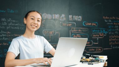 Kara tahtada dizüstü bilgisayar kullanarak akıllı kız programlama sistemi. Lise öğrencisi mühendislik kodları yazıyor ya da STEM teknoloji sınıfında kameraya bakarken bir şey söylüyor. Yaratıcı eğitim. Öğretim.