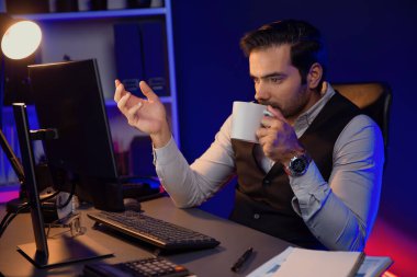 Gülümseyen zeki işadamı, elinde kahve fincanı olan satış ekibiyle buluşuyor ve geceleri Mor Neon Light Home Office 'deki bilgisayar ekranında ürün hedef pazarını araştırıyor. Tahmin et..