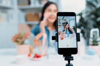 Seçici odak akıllı telefonu ile genç ve güzel Asyalı makyaj fırçası yanak testi koleksiyonunu pastel renkli, sosyal medyada tanıtım yapmak için ışıldayan bir ruh hali gösteriyor. Taktik.