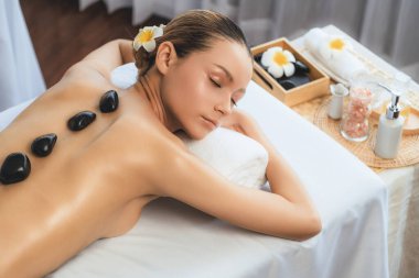 Lüks tatil köyündeki kaplıcalarda sıcak taş masajı. Gün ışığı sükunet ortamında, mutlu kadın müşteri bazalt taş masajından zevk alıyor. Rahatlatıcı bir sıcaklıkla vücudun üzerinde süzülüyor. Sessiz.