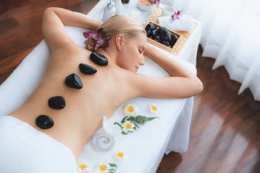 Lüks tatil köyündeki kaplıcalarda sıcak taş masajı. Gün ışığı sükunet ortamında, mutlu kadın müşteri bazalt taş masajından zevk alıyor. Rahatlatıcı bir sıcaklıkla vücudun üzerinde süzülüyor. Sessiz.