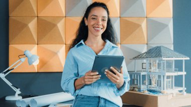 Genç, güzel İspanyol mimar mühendis modern ofisteki ev modeli yapısını kontrol ederken tablet kullanarak bina inşaatını çiziyor. Yaratıcı iş inşaat konsepti. Yönlendirici.