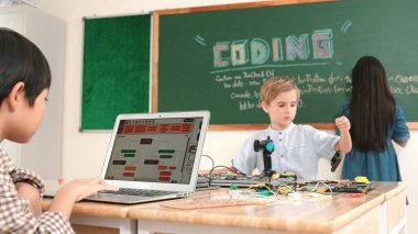 Kafkas arkadaşı STEM sınıfında elektrik panosunu tamir ederken Asyalı çocuk kodlama programı. Enerjik öğrenci kodlama mühendisliği komut yazarken ve yapay zeka yazılımını programlarken tahtada duruyor. Pedagoji.