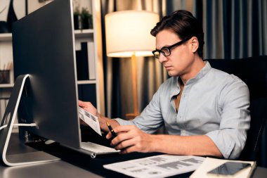 Akıllı iş adamı iş paragrafı dinamik pazarlama analizi planını analiz ediyor. Kağıt kağıtları ve bilgisayar monitörü raporlarını gece evdeki belge verileriyle karşılaştırmak için hazırlıyor. Bireysel.