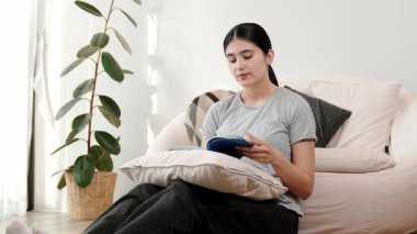 Kanepede oturan bir kadın ders kitabı okuyarak sosyal ve mesleki teknoloji bilgisini artırır ya da akıllı bir anne olmak için çocuk yetiştirir. Hayat boyu öğrenme konsepti. Uyumsuzluk.