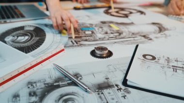 Karmaşık bir teknik diyagrama odaklı, işbirlikçi bir mühendislik çalışma alanı. Araçlar ve kağıtlar dağınık vaziyette dizayn ve planlama sürecini gözler önüne seriyordu. SACTR