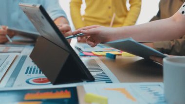 Çeşitli profesyonellerden oluşan bir grup, strateji ve fikirleri tartışırken, dijital tablet üzerindeki çizelge ve verileri analiz ederek ortak bir iş toplantısı düzenliyor. SACTR