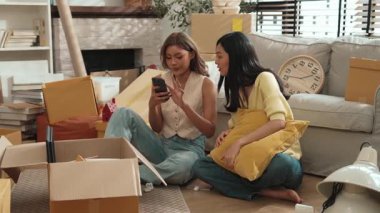 Oturma odasında kutuları etrafa saçılmış bir şekilde oturan bir arkadaş telefona bakıp duruyor. Taşınırken birlikte zaman geçirirken telefona bakan mutlu ev arkadaşı ya da lezbiyen çift. Myrmidon.