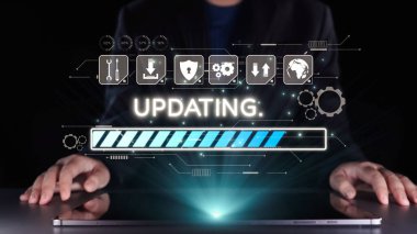 Bir iş adamı, sistem güncellemelerini izlerken dizüstü bilgisayarla etkileşime girer, teknolojinin gelişimini sembolize eden parlak bir ilerleme çubuğu ve dijital arayüz unsurlarını gösterir. Dörtgen