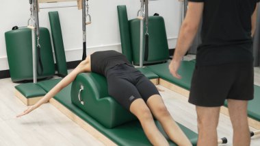 Happy Pilates eğitmeni, bir müşteriye yay namlu teçhizatı kullanarak çekirdek güçlendirme egzersizinde rehberlik ediyor. Çekici kadın bacak esnetme pozu veriyor. Vücut ve denge çalışması için, kas gücünü arttırmak için. Alışkanlık.