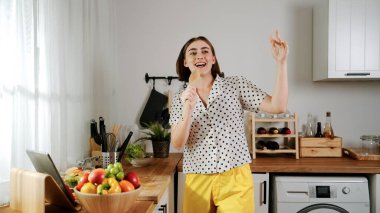 Enerjik beyaz anne kahvaltı için salata pişirirken ve yemek pişirirken elinde kepçeyle şarkı söylüyor. Sağlıklı yemek yapmaya hazırlanırken müziğe yönelen mutlu ev sahibi. Pedagoji.