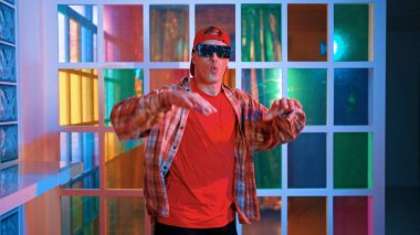 Komik break dansçı kameraya bakarken hiphop 'a doğru serbest adım atıyor. Çılgın mutlu hipster dans edip sokak dansı yaparken Led ışığında günlük kıyafet ve güneş gözlüğü takıyor. Mutluluk.