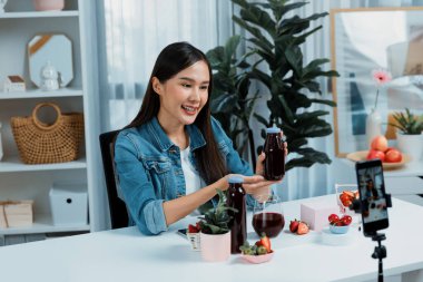 Gülümseyen, güzel Asyalı genç, lezzetli karışık çilek ve kiraz suyu detoksu içeceklerini inceleyen, sosyal medyada özel promosyon satışı için sağlıklı ürünler sergileyen. Taktik.