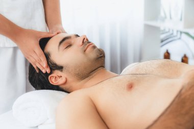 Beyaz adam stres önleyici kafa masajından ve lüks bir tatil beldesi veya otel spa salonundaki modern ışık ortamında yüz güzelliği eğlencelerini şımartmaktan hoşlanıyor. Sessiz.